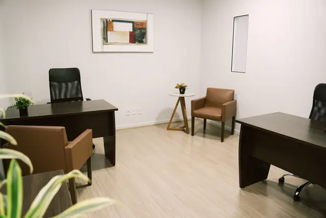 Sala 206 da Willtay em Brusque: duas mesas de trabalho em madeira escura, poltronas e armários baixos